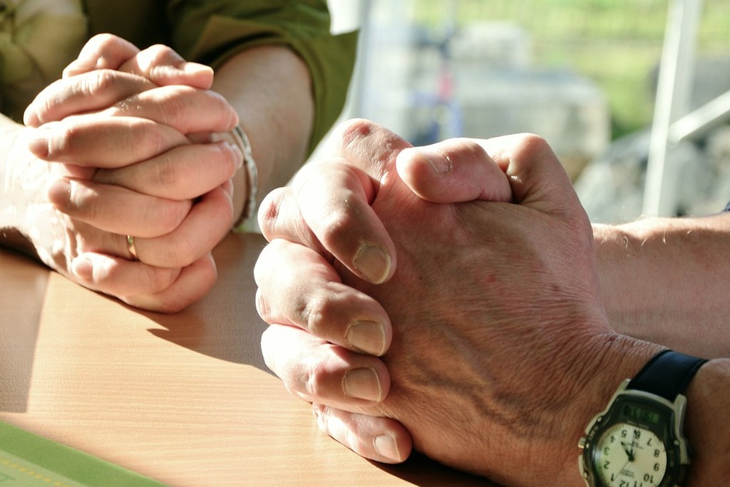 Zwei Personen beten und haben die gefalteten Hände auf einem Tisch abgelegt.
