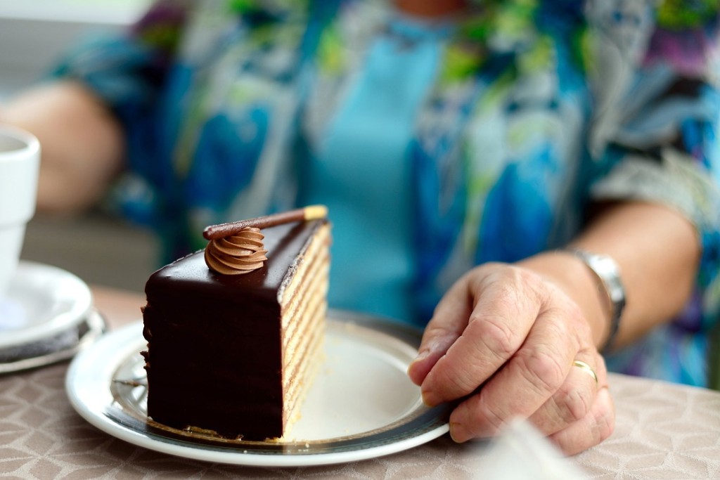 Auf dem Tisch steht ein Stück Schokotorte. Dahinter sitzt eine ältere Person.