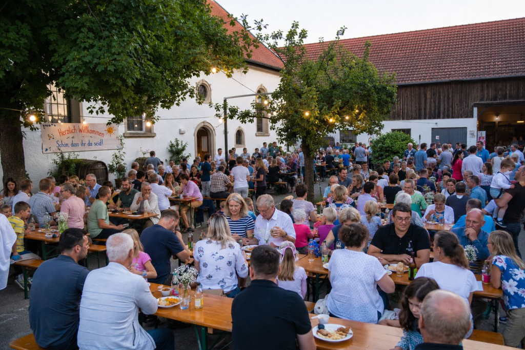 Viele Menschen sitzen auf einem Hof an Biertischen und -bänken und feiern gemeinsam.